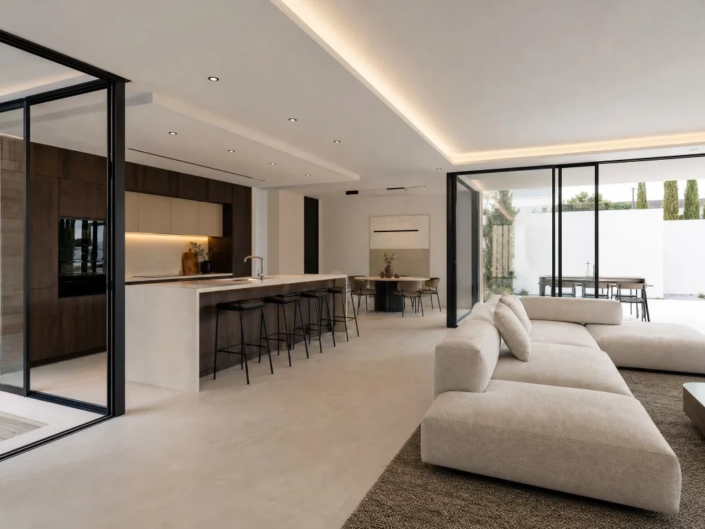 Vista interior de un salón comedor diáfano de lujo en una vivienda modular de hormigón con iluminación LED empotrada.